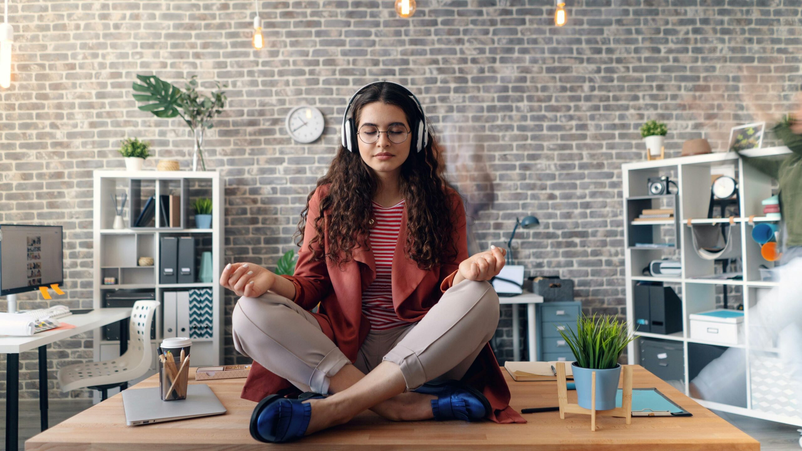 Kako je mindfulness postao ključ uspeha u modernom poslovanju 1 Young woman meditating with headphones in a modern office setting, practicing mindfulness.